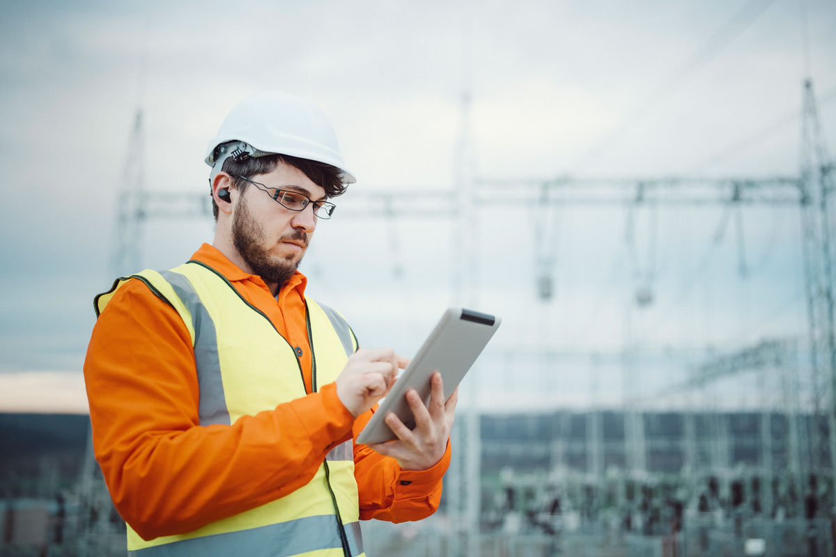 Ingenieur mit Tablet vor einer Stromtrasse