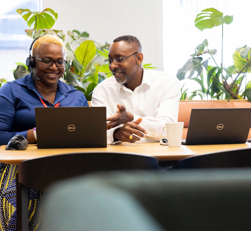 A man and woman sitting at a table with laptops, working together on a project.