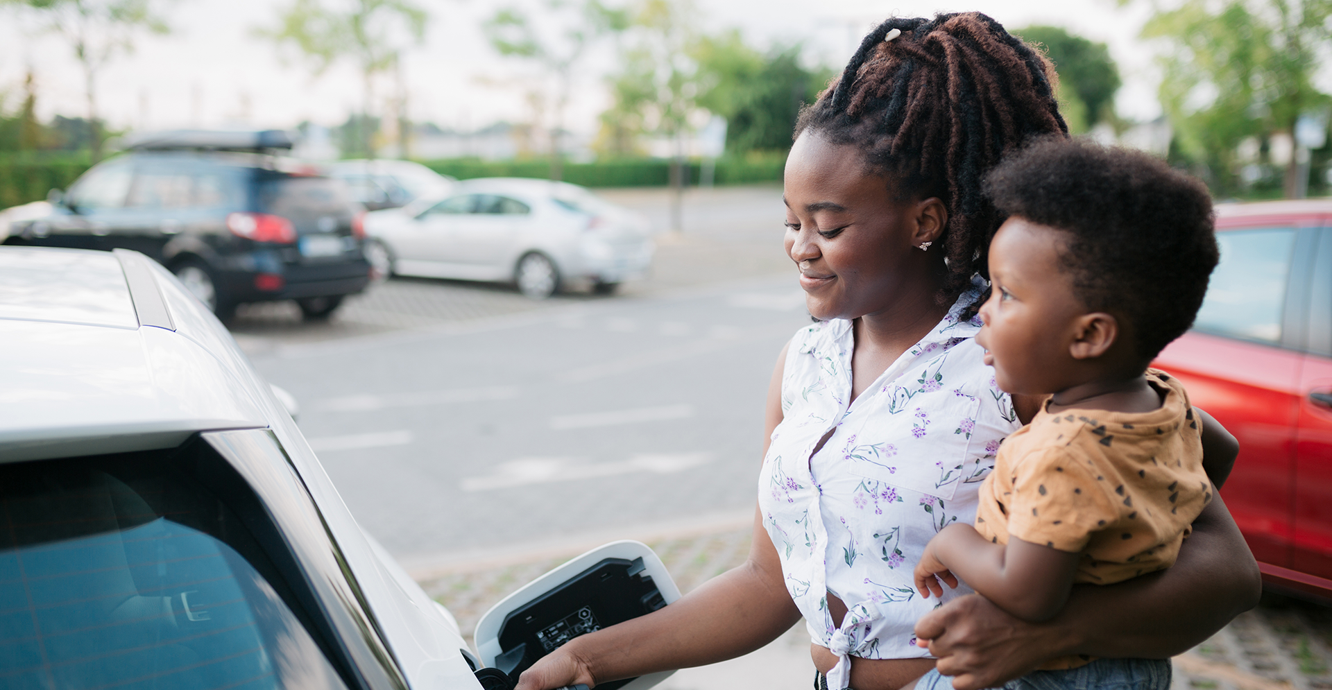 Mother holding her son while charging her electric vehicle